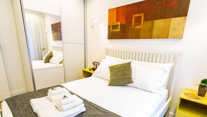 A hotel room with a neatly made bed, a bedside table with a plant, and a mirror on the wall. - Apartamento 2 Quartos - Praça Pôr do Sol (São Paulo)