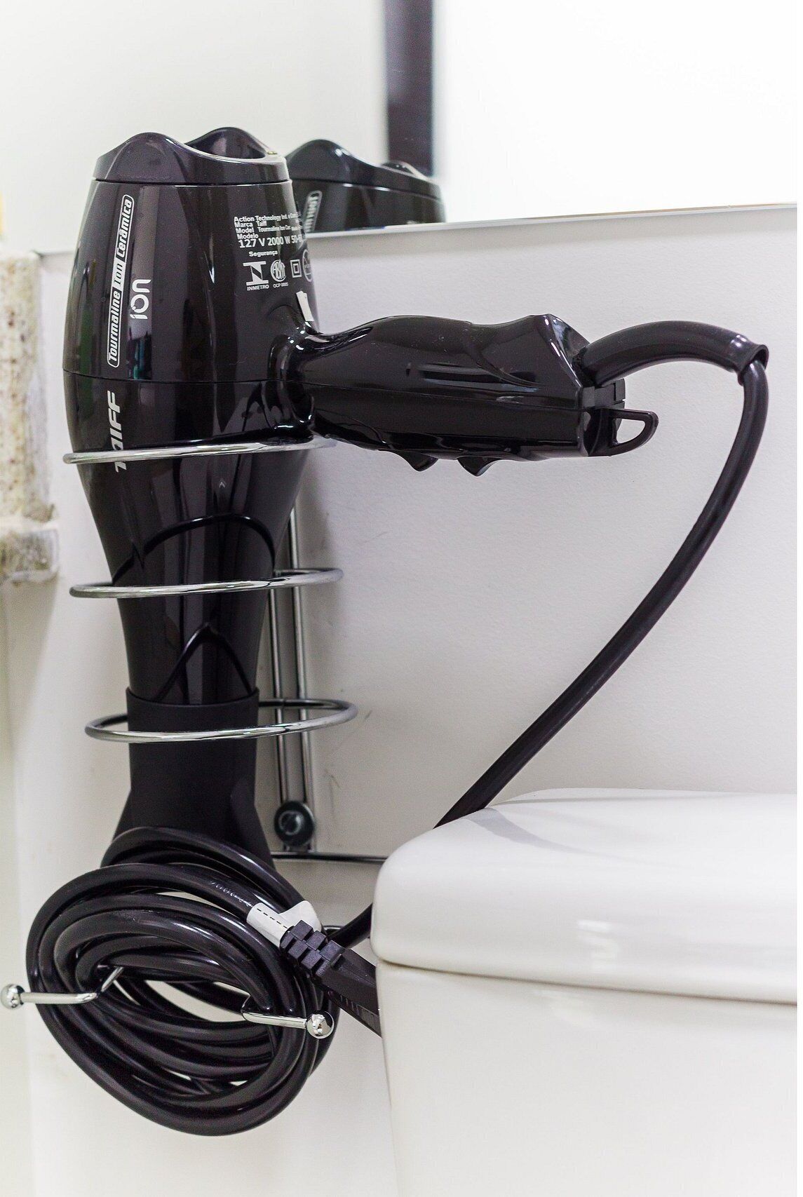 A black hairdryer mounted on a white wall, connected to a power outlet.