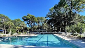 Una piscina rectangular con agua azul cristalina, rodeada de árboles y un pabellón cubierto.