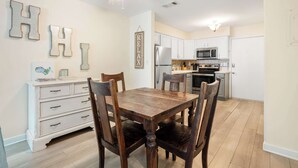 Un comedor con una mesa y sillas de madera, un aparador blanco y una cocina al fondo.