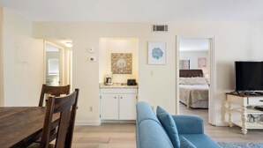 Una habitación con una mesa de comedor, un sofá azul, un televisor y una kitchenette.