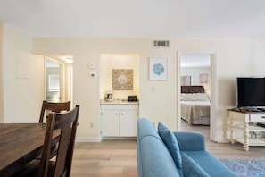 Una habitación con una mesa de comedor, un sofá azul, un televisor y una kitchenette.