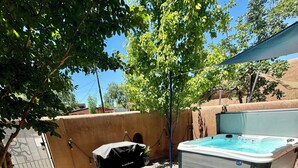 A backyard with a hot tub, a barbecue grill, and a tree providing shade.