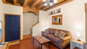 A living room with a brown leather sofa, a wooden coffee table, a blue door, and a staircase in the background.