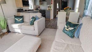 A modern living room with a sofa set, a coffee table, and a kitchen area in the background. - 62 Pinewood (Mablethorpe)