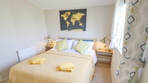 A neatly arranged bedroom with a large bed, two bedside tables with lamps, a world map on the wall, and a radiator. - 62 Pinewood (Mablethorpe)
