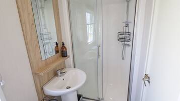 Casa de banho com cabine de duche em vidro, lavatório branco e espelho sobre o lavatório.