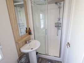 Casa de banho com cabine de duche em vidro, lavatório branco e espelho sobre o lavatório.