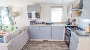A compact kitchen with grey cabinets, a built-in microwave, a stove, and a sink. - 62 Pinewood (Mablethorpe)