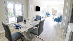 A modern dining area with a wooden table, black chairs, and a TV mounted on the wall. - Southend (Malvern)