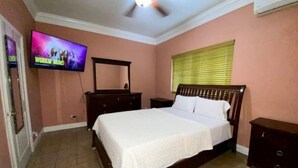 A bedroom with a bed, a dresser, a nightstand, a TV, and a ceiling fan.