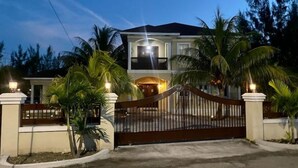 A two-story house with a gated entrance, surrounded by palm trees and a well-maintained lawn.