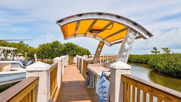 Een houten terras met een gebogen metalen overkapping, omringd door water en begroeiing.