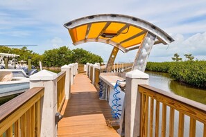 A wooden deck with a curved metal canopy, surrounded by water and greenery. - Bayside Condo with Pool and Dock (Key Largo)
