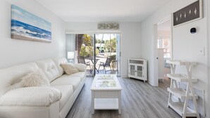 Een moderne woonkamer met een witte bank, een salontafel met glazen blad en uitzicht op het buitenterras.
