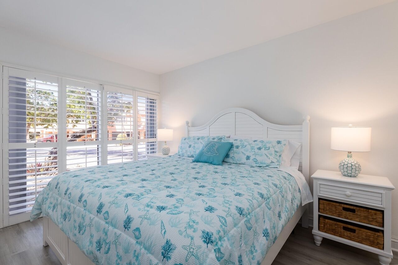 A bedroom with a bed, a nightstand, and a window with blinds.