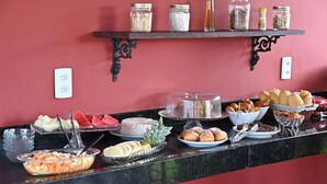 Ein Buffet mit verschiedenen Speisen, darunter Obst, Gebäck und Desserts, präsentiert auf einer Marmorplatte vor einer roten Wand.