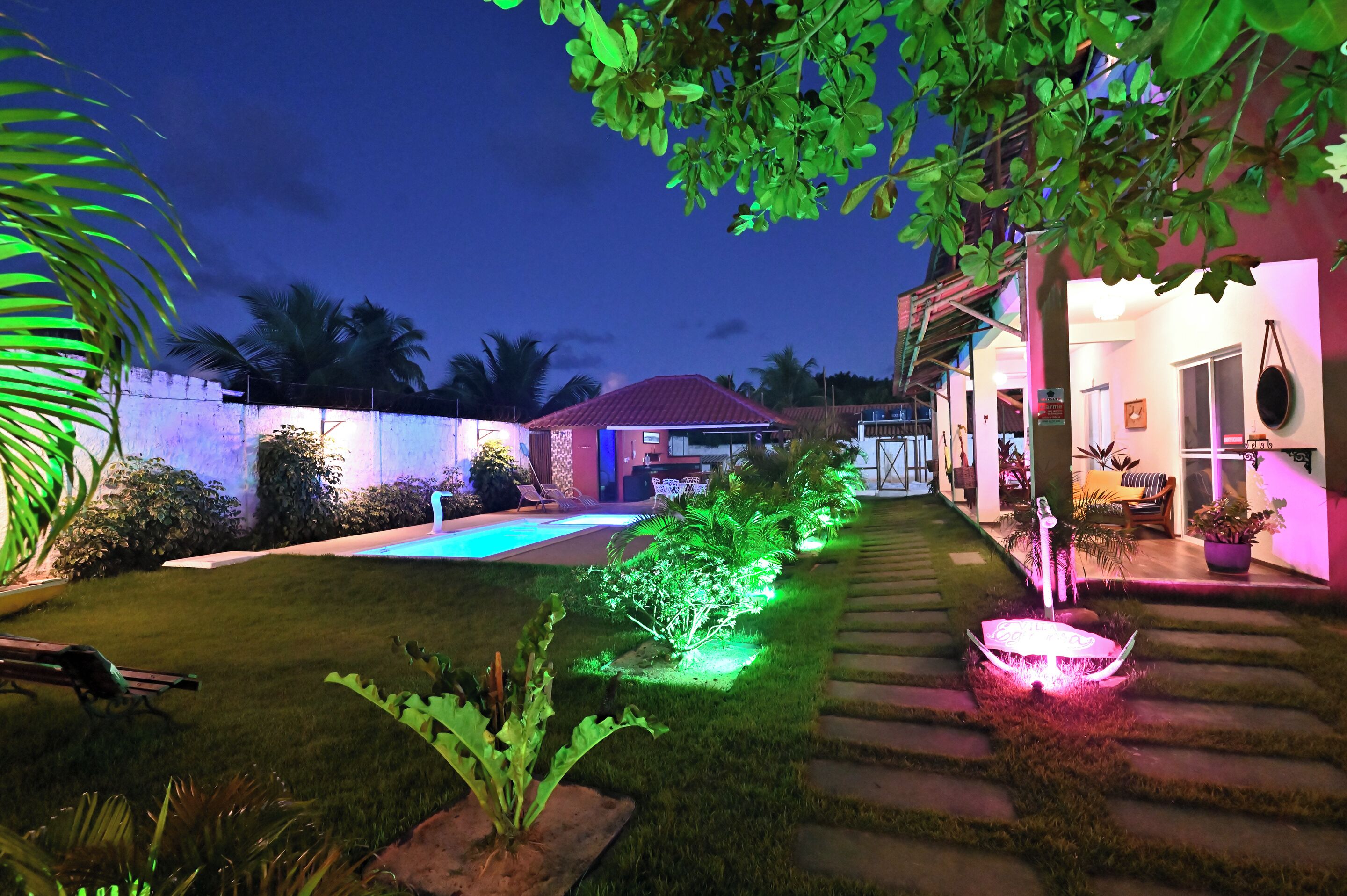 A well-lit backyard with a swimming pool, a patio area, and a house with a red roof.