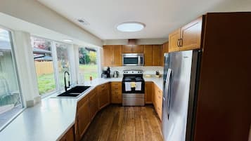 A modern kitchen with wooden cabinets, stainless steel appliances, and a large window providing a view of the outdoors.