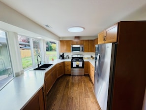 A modern kitchen with wooden cabinets, stainless steel appliances, and a large window providing a view of the outdoors.