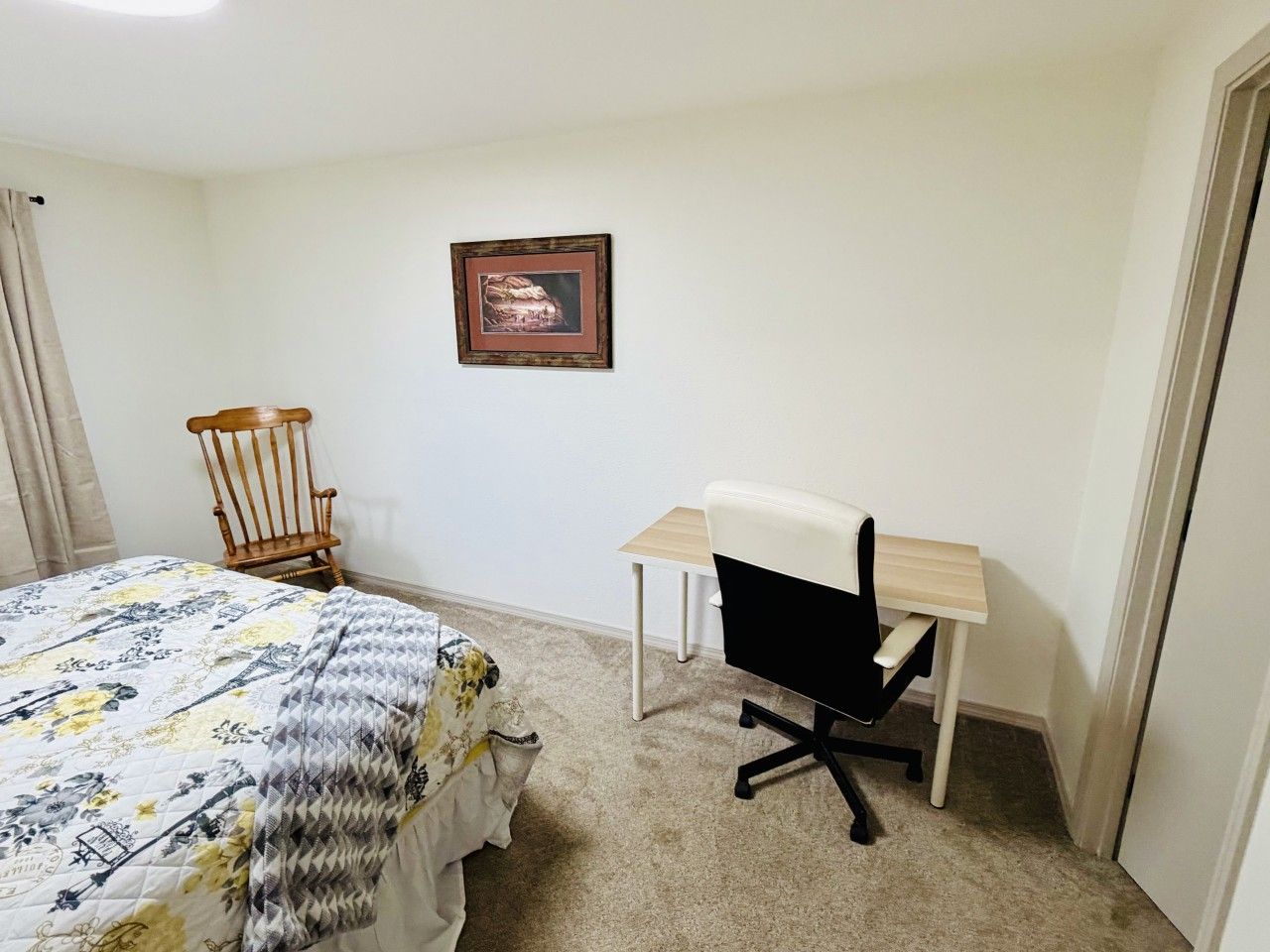 Une chambre à coucher avec un lit, un bureau, une chaise, une chaise en bois et un tableau encadré accroché au mur.