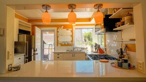 Une cuisine moderne dotée d’un grand îlot central, de luminaires suspendus et offrant une vue sur l’extérieur.