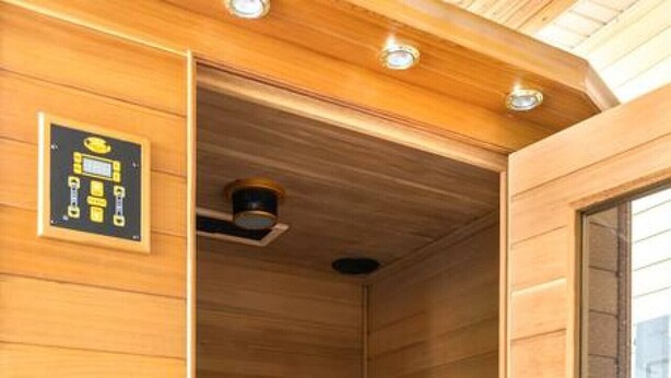 Een sauna met houten wanden en een glazen deur, met een bedieningspaneel en planken voor handdoeken.