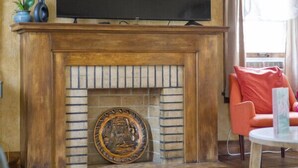 A living room with a fireplace, a flat-screen TV mounted above it, a red chair, and a small table.