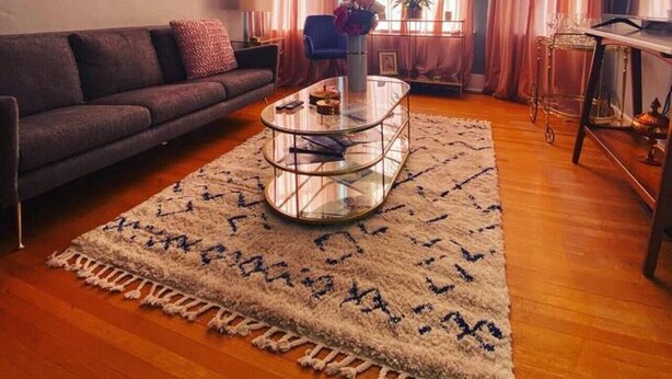 Ein Wohnzimmer mit Sofa, einem Glastisch, einem Teppich, einem Bild an der Wand und einer Chandelier.