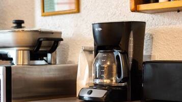 A kitchen with a coffee maker, a kettle, and a shelf with condiments.
