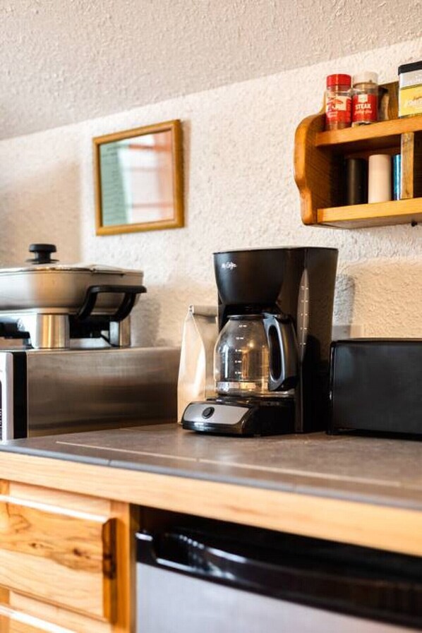 Una cocina con cafetera, hervidor y estante con condimentos.