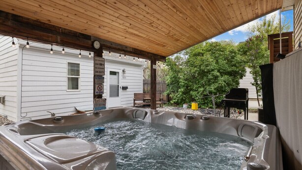 Ein Whirlpool unter einer Holzpergola, im Hintergrund ein weißes Haus.