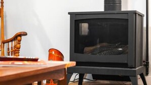 A room with a black wood-burning stove, a wooden chair, and a table with a box of matches. - Bo’s Old West Abode with Hot Tub and Sauna (Billings)