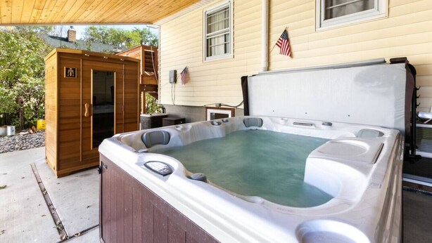 Ein Whirlpool vor einem Haus mit einer Holzterrasse und einem kleinen Gartenhaus.
