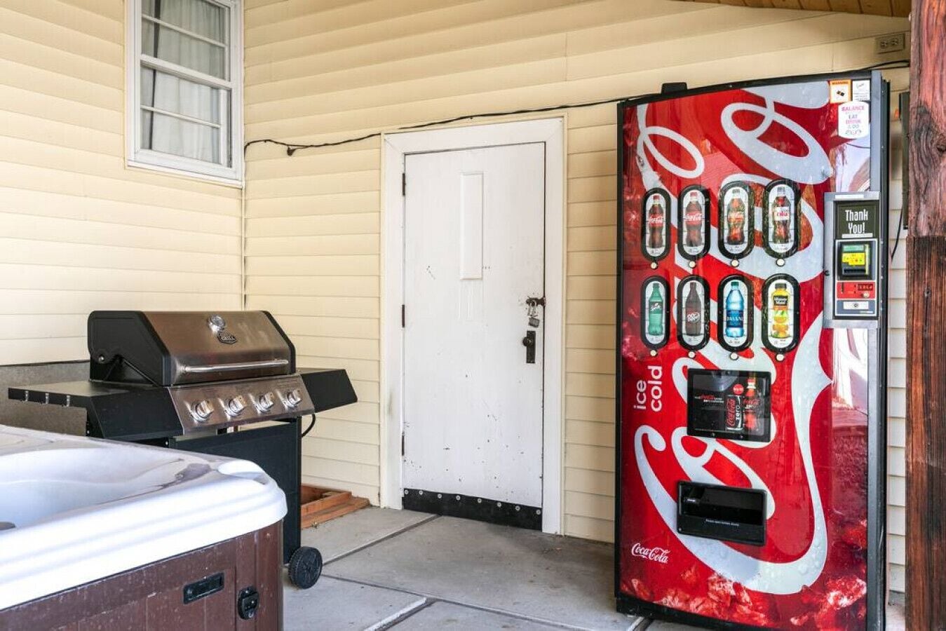 A Coca-Cola vending machine, a grill, and a door in front of a house.
