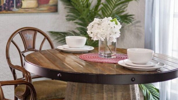 A dining table with white bowls and a vase of white flowers, surrounded by wooden chairs.