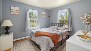 A bedroom with a bed, a bedside table, a lamp, a window, and a vase with flowers.