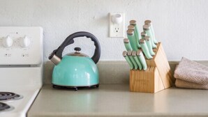 A kitchen with wooden cabinets, a white stove, a teal kettle, and a knife block.