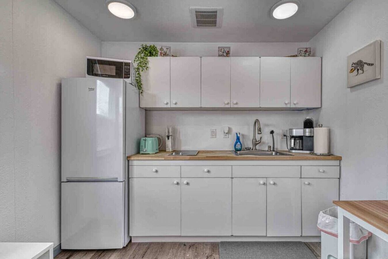 A compact kitchen with white cabinets, a microwave, a toaster, a sink, and a coffee maker.