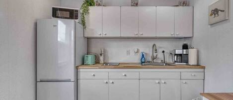 A compact kitchen with white cabinets, a microwave, a toaster, a sink, and a coffee maker.