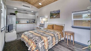 Quarto com cama, mesa de cabeceira e vista para uma cozinha.