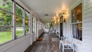 A covered porch with large windows, a wooden floor, and a chair. - Historic Manor, sleeps 10+, 5 Bedroom, huge yard, lake, fishing, parks, events
 (Winter Haven)