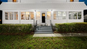 A two-story white building with a staircase leading to the entrance, surrounded by well-maintained hedges. - Historic Manor, sleeps 10+, 5 Bedroom, huge yard, lake, fishing, parks, events
 (Winter Haven)