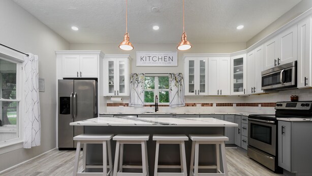 A modern kitchen with white cabinets, stainless steel appliances, and a marble island with bar stools. - Historic Manor, sleeps 10+, 5 Bedroom, huge yard, lake, fishing, parks, events
 (Winter Haven)