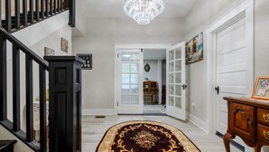A hallway with a chandelier, a wooden staircase, and a patterned rug. - Historic Manor, sleeps 10+, 5 Bedroom, huge yard, lake, fishing, parks, events
 (Winter Haven)