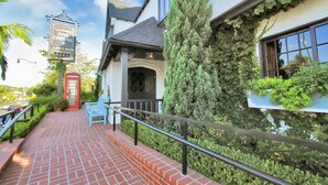 A brick pathway leading to a building with a red door, a sign for 'Five Crowns', and a large tree. - CDM Beach House (Newport Beach)