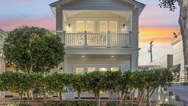 A two-story house with a balcony, surrounded by trees and a sunset in the background. - CDM Beach House (Newport Beach)