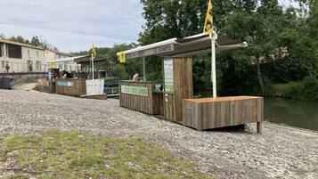 A riverside kiosk with wooden structures and a sign indicating a bar and canteen.
