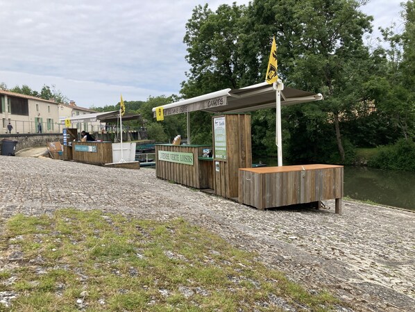 Ein Flussufer-Kiosk mit Holzbauten und einem Schild, das Bar und Imbissbetrieb anzeigt.