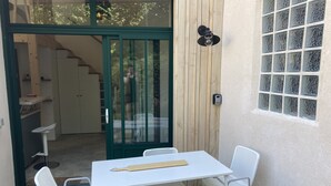 A small outdoor seating area with a table and two chairs, a wooden door, and a window with frosted glass. - Le Refuge des Bateliers (Arçais)